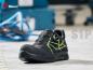 Preview: The image shows a black safety shoe with yellow accents and a reinforced toe. It is standing on a gray floor in a workshop environment.