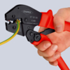 Preview: The image shows a hand holding a pair of wire cutters. The pliers have red handles and a black cutting surface, into which a green and yellow cable is inserted.