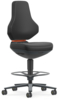 Preview: The chair has a high, ergonomic backrest and a padded seat in black. It is mounted on a mobile base with a round foot ring. An orange accent is visible.