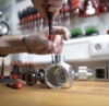 Preview: A hand with a screwdriver repairs a metallic part on a wooden table. In the background, various tools and a tool holder are visible.