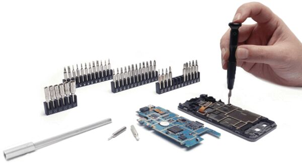 The image shows a hand holding a screwdriver and working on an electrical circuit board. Next to the board, various screwdriver bits and tools are arranged.