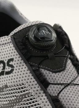 The image displays a gray sports shoe. At the top, there is a black lacing system with a round click mechanism. The shoe features a breathable mesh material.