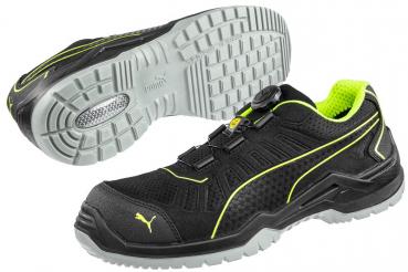 The image shows a black sports or safety shoe with yellow accents. It has a textured sole and a quick lacing system. The upper part is designed to be breathable.