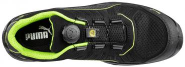 The picture shows a black sports shoe with yellow accents. The shoe features a quick lacing system and a breathable texture. It is designed to be modern and functional.