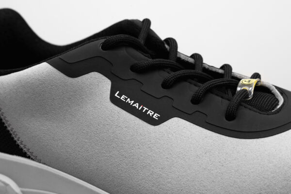 The image shows a close-up of a sports shoe. The shoe has a gray upper with black details and laces. On the side, there is the "Lemaitre" logo.