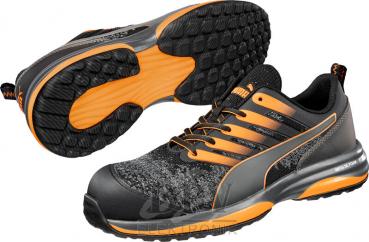 The image shows a pair of sports or casual shoes. They are black with gray and orange accents. The sole has a non-slip tread and the shoes appear modern and sporty.