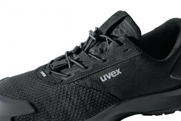 The image shows a black sports shoe with a modern, simple design. The surface is made of a breathable material, and the laces are clearly visible. The "uvex" logo is visible.