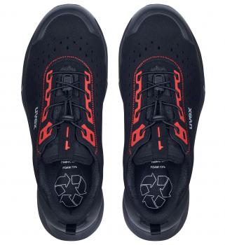 The image shows a pair of athletic shoes in black with red accents. The surface has numerous ventilation holes. They are equipped with lacing and have a distinctive, non-slip sole.