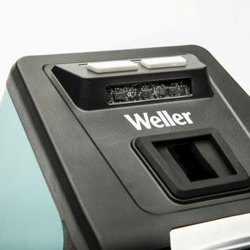 The image shows an electronic station with a dark surface and a Weller logo. At the top, there are two white buttons and a small screen. At the bottom, there is a rectangular opening.