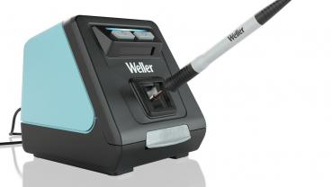 The image shows a soldering station with a black casing and a turquoise side. A soldering iron is inserted into a holder. The brand "Weller" is clearly visible.