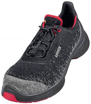 The shoe is a sports or running shoe in black with a textured surface. It has red accents and a gray, soft toe area. The laces are elastic and ensure a secure fit.