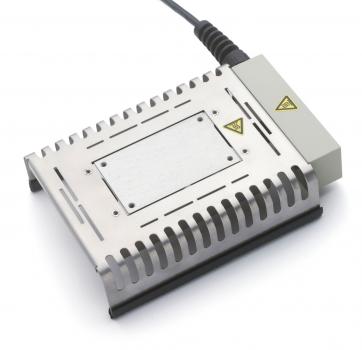 The image shows a rectangular, silver-colored device with cooling fins and an attached cable connection. It has a smooth, flat surface in the middle and yellow warning symbols.