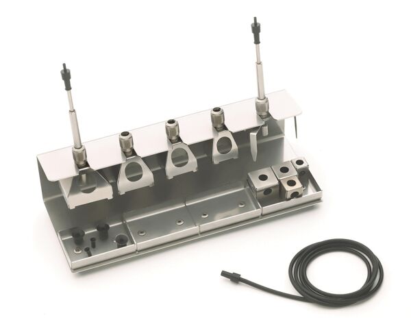 The image shows a metallic tool set with several holders and connections. There are three upright elements and a cable connection that runs sideways. The surface is flat.