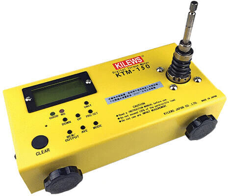 The image shows a yellow, rectangular measuring device with a digital display, buttons, and an antenna connection on top. It has two round, black feet on the bottom.