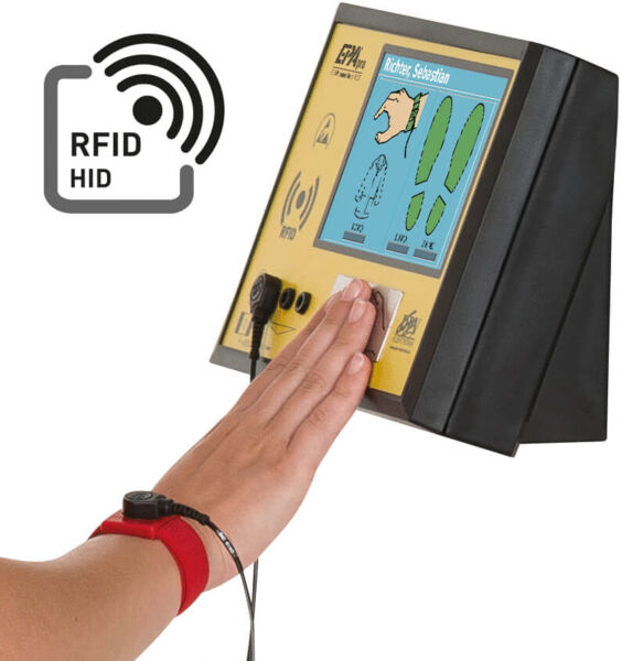 Das Bild zeigt ein Gerät mit einem Touchscreen, das zur Erkennung von RFID-Chips verwendet wird. Eine Hand mit einem roten Armband steht nah am Bildschirm, der verschiedene Symbole zeigt.