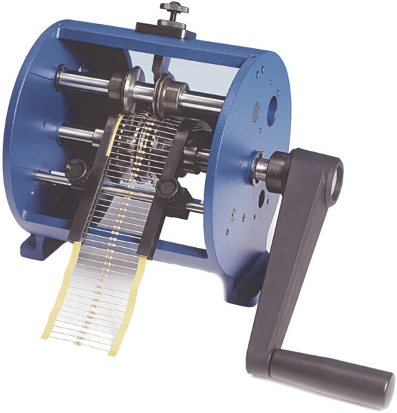 The image shows a mechanical machine with a blue casing and a crank. Inside, there are several rotating rollers that work with striped belts to perform processing steps.