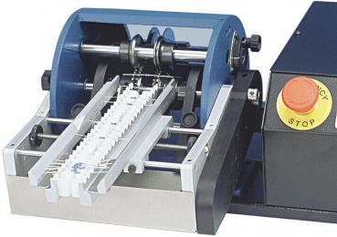 The image shows a machine for milling or cutting. It has two large rollers that rotate, and a long chute for the material. On the right side, there is an emergency stop button.