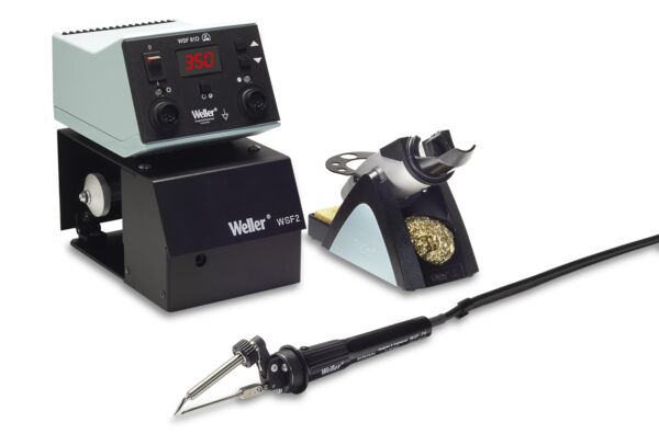 The image shows a soldering station with a digital temperature controller on top, a black base, and a soldering iron on the left side. On the right, there is a holder with cleaning wool.