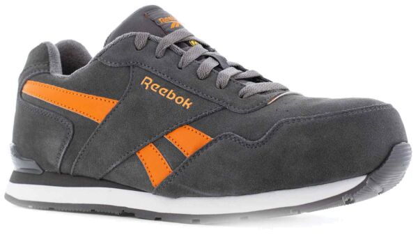 Der Schuh ist ein grauer Sneaker mit orangen Akzenten. Er hat eine strukturierte Oberfläche, eine klassische Schnürung und eine weiße Sohle. Das Logo ?Reebok? ist auf die Seite gedruckt.