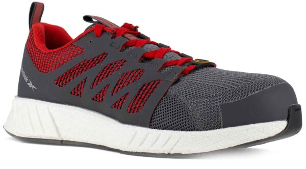 The shoe is sporty, mostly gray with red accents. It features a breathable mesh material, a solid toe cap, and a white, textured sole. The laces are red.