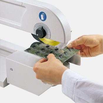 In the picture, you can see a person holding a circuit board with one hand. The other hand is operating a machine with a large, round blade that hovers over the circuit board.