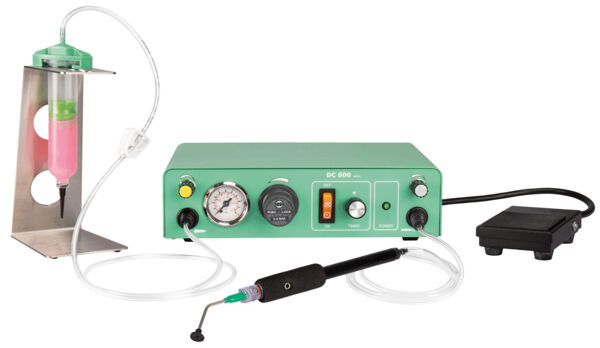 The image shows a medical device. It has a green casing with a pressure gauge and switches. A hose leads to a handpiece with a fine nozzle, next to it there is a foot pedal and a container with liquid.