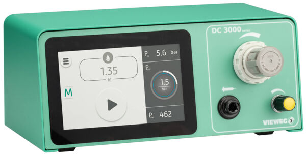 The image displays a green device featuring a large touchscreen. The display shows numerical values and symbols, including pressure readings. On the side, there are rotary and push buttons.