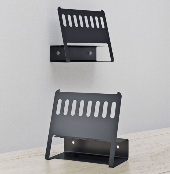 The image displays two simple, black metal shelves on a wall. They are mounted at different heights and feature striking, straight lines with holes on the top surface.