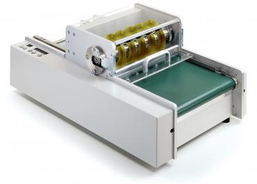 The image shows a device with a long, narrow casing in white. It has a green conveyor belt surface and a transparent roller visible at the top.