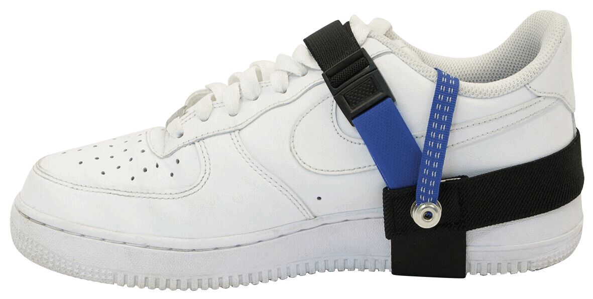 The image shows a white sneaker with a flat sole. On the outside of the shoe, there is a black and blue strap attached that serves for stabilization.