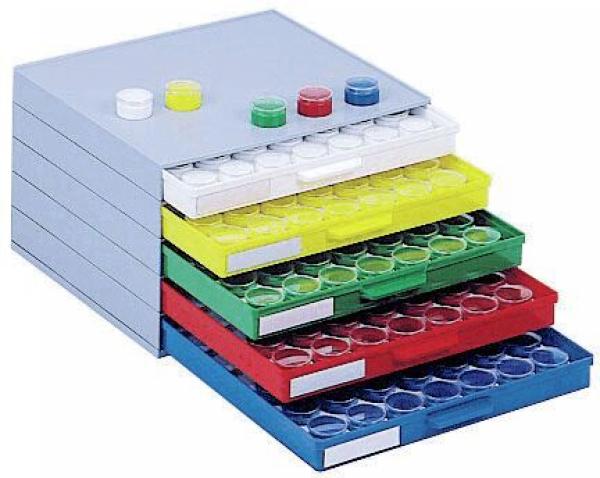 The image shows a stackable box with five drawers in different colors – Gray, Yellow, Green, Red, and Blue. Each drawer has openings for small, round containers.