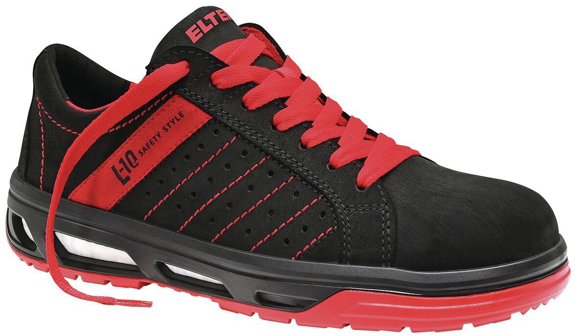 The shoe is a black sneaker with red accents. It has a flat sole and laces. There are line patterns on the side and the logo is clearly visible. It looks sporty and modern.