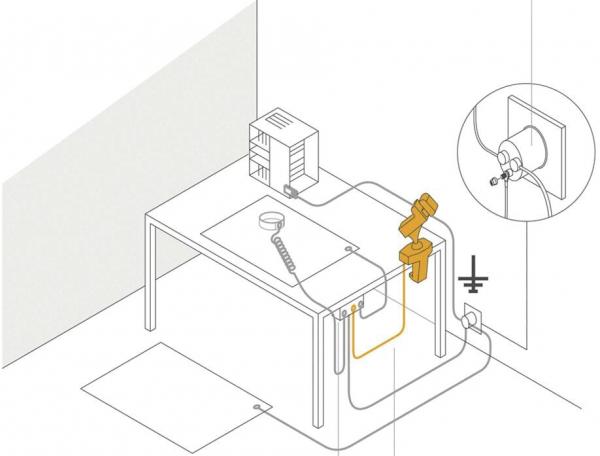 The image shows a table with a machine, a container, and a robotic arm. Cables connect the devices. An outlet is depicted on the side.