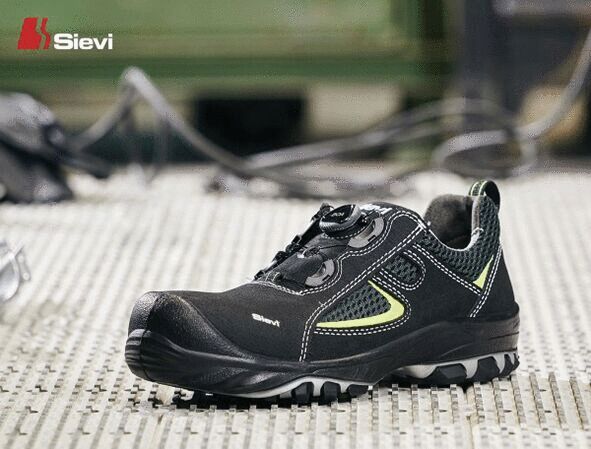 The image shows a black safety shoe with striking yellow details. It has a sturdy rubber sole and a sporty cut, ideal for industrial environments.