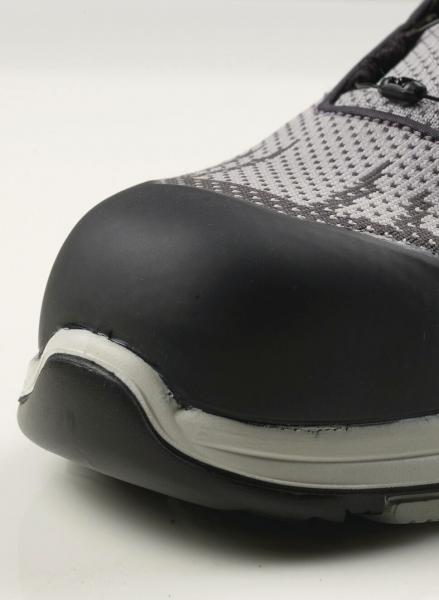 The image displays the front of a sports shoe. The toe cap is black and prominent, while the upper is made of gray, mesh-like material. The texture is smooth.