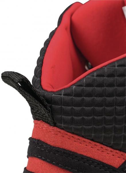 The image displays the upper part of a sports shoe. The surface is black with a textured texture, while the lining is red. Black stripes run along the side.