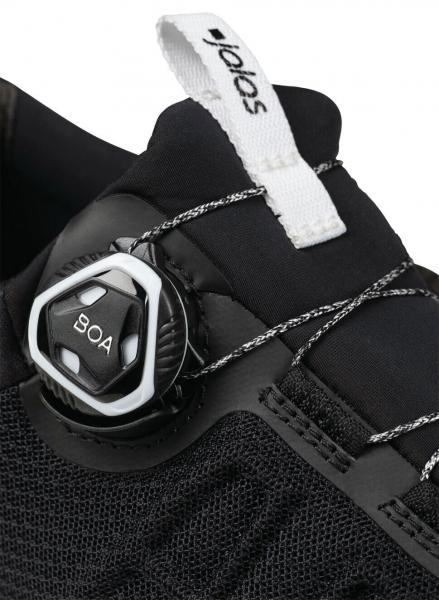 The image shows part of a black shoe with a rotary closure system. The shoe has a textured surface and white lettering on top.