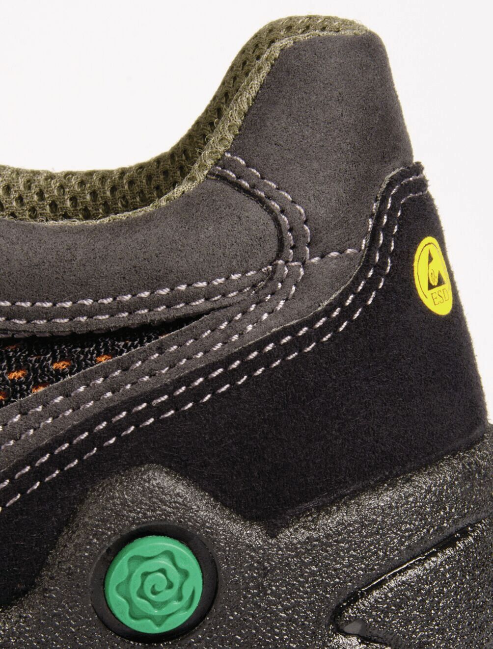 The image shows a black shoe with gray upper and green sole. It features lacing and prominent, yellow branding. The texture appears sturdy and athletic.