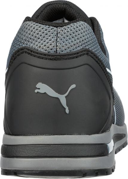 The image displays the rear view of a modern sport shoe in black and gray. The material is breathable, and a gray Puma logo is prominently visible on the heel.