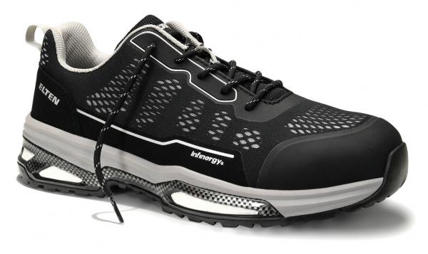 The shoe is black with gray and white accents. It has a modern design, a padded sole, and many small holes for ventilation. The laces are black.