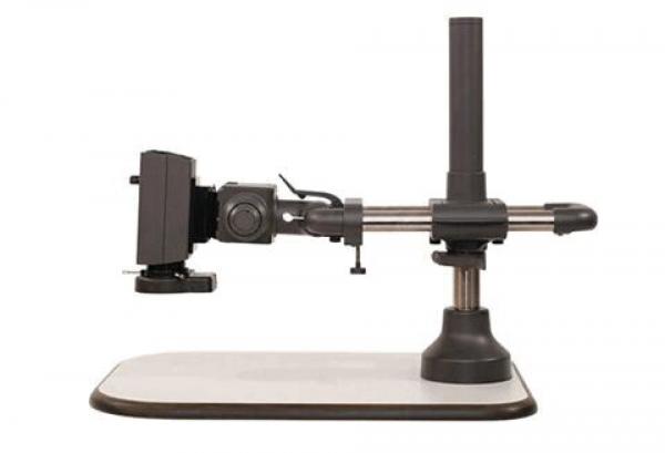 The image shows an optical device on a stable, rectangular table. It has a gray base, a vertical support, and an arm structure with a holder for lens-like objects.