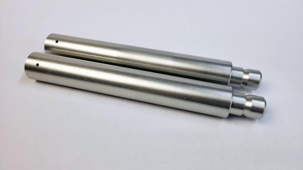 The image shows two elongated, silver metal cylinders lying parallel to each other. They have a smooth surface and a larger diameter at one end.