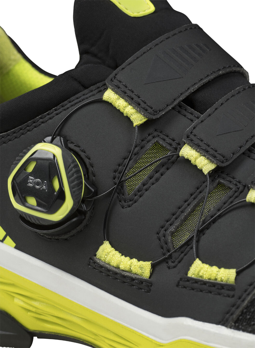 The image shows a sporty shoe in black with neon accents. It features a modern closure mechanism and wide Velcro straps for good support.