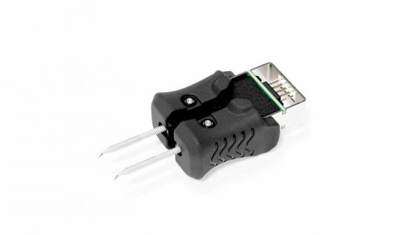 Das Bild zeigt einen schwarzen Adapter mit einem USB-Stecker an einem Ende und zwei Stiften am anderen Ende. Der Adapter hat eine gummierte, strukturierte Oberfläche für besseren Halt.