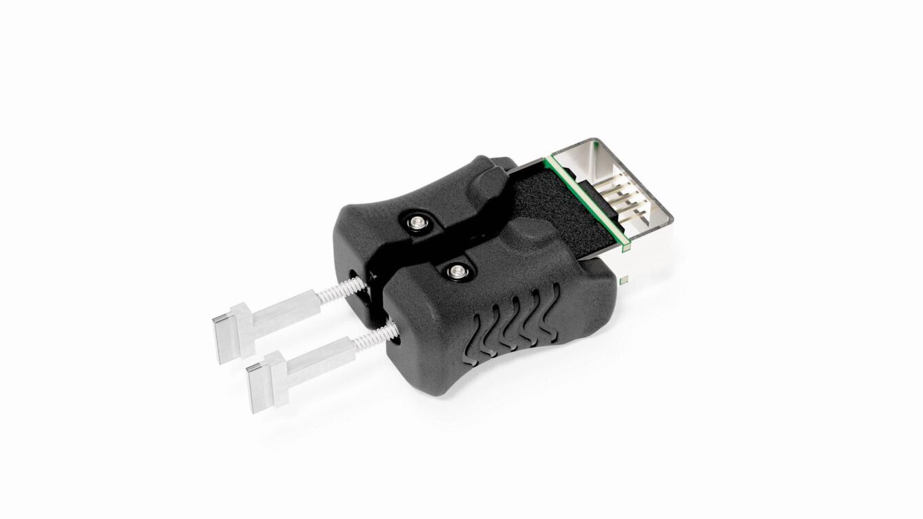 The image shows a black adapter with two silver pins protruding forward. At the top, a connection is visible, displaying a green and black area.