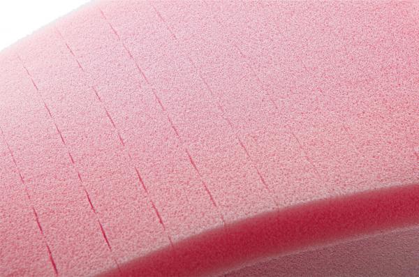 The image shows a pink foam surface with fine, parallel grooves. The structure is soft and has a slightly curved shape. It conveys a sense of flexibility.