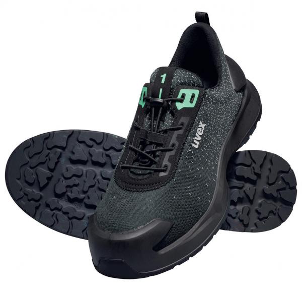 The image shows a black sports shoe with a smooth surface and green laces. The sole has a textured profile for good grip. The shoe looks modern and functional.