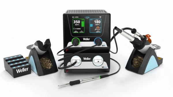 The image shows a soldering station with a control unit and two soldering tips. The control unit has a display with temperature readings. Next to the unit, there are soldering tin and cleaning materials.