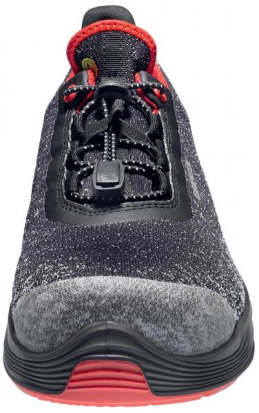 The shoe is sporty, with a gray upper and a black mesh part. The laces are black, with a red accent at the top edge. The sole is black with a red bottom.