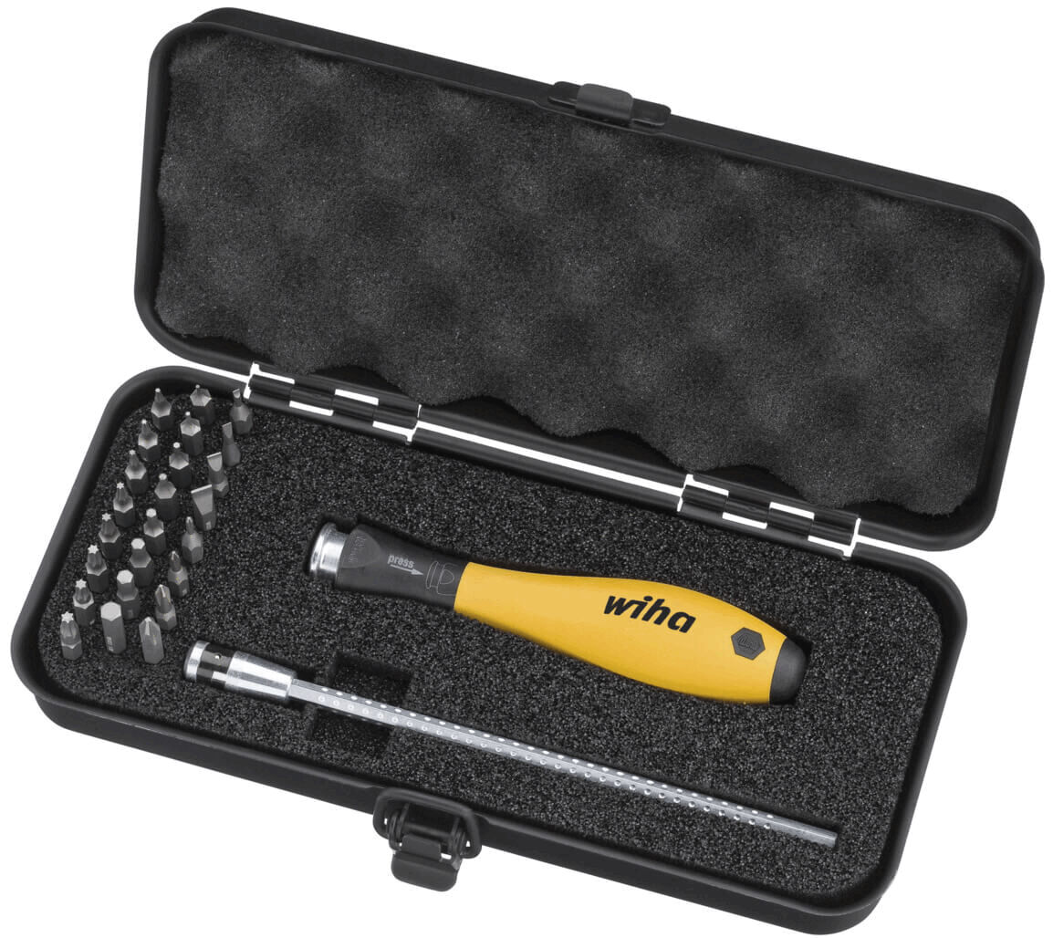 The image shows a black box with foam-padded interior. Inside, there is a yellow screwdriver and various removable bits.